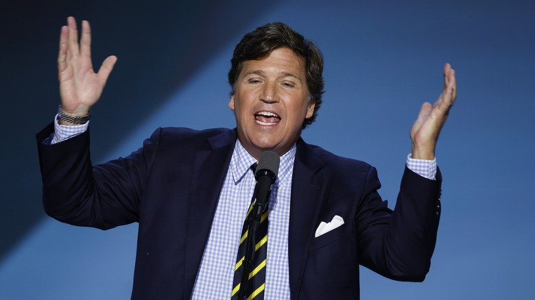 Tucker Carlson throwing his hands in the air as he talks into mic