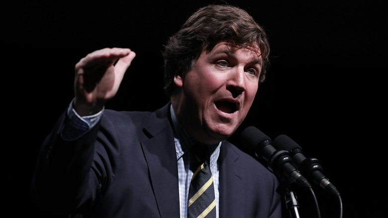 Tucker Carlson appearing to speak loudly into a microphone