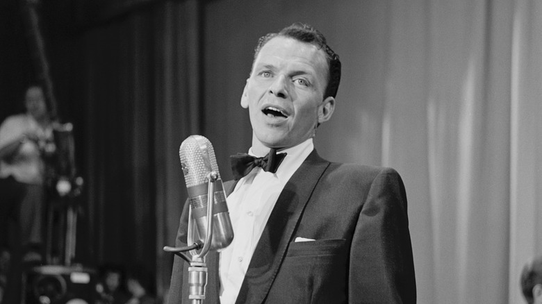 Frank Sinatra singing into a microphone onstage in black and white.