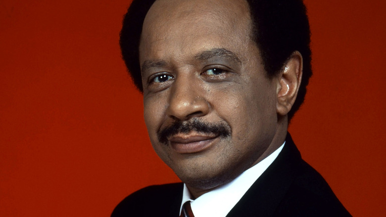 Sherman Hemsley in front of a red backdrop