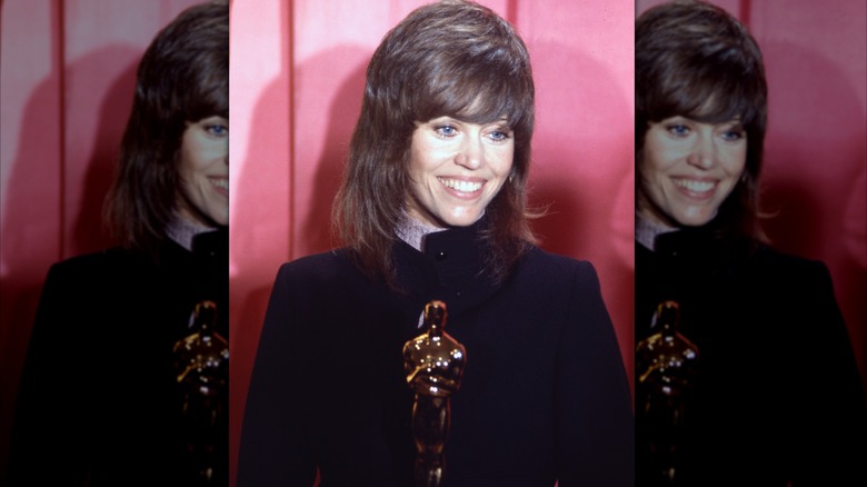 Jane Fonda smiles as she holds her first Oscar Award against a pink backdrop