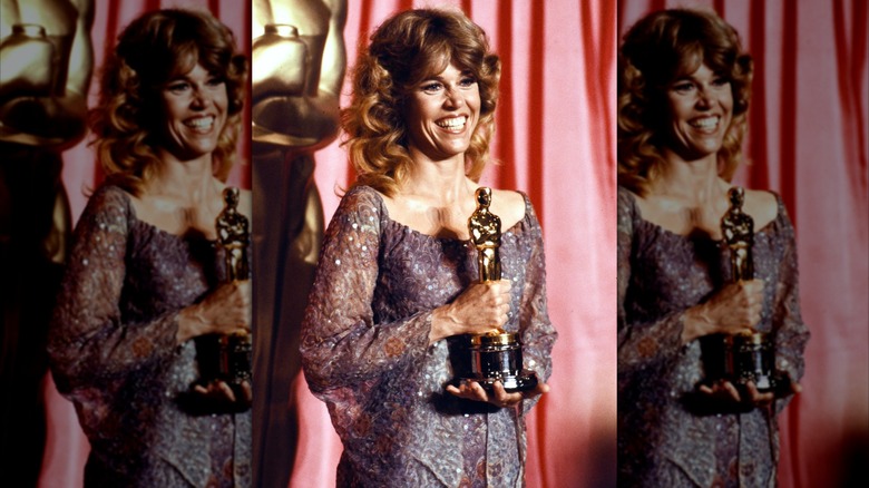 Jane Fonda smiles and holds her second Oscar Award against a pink backdrop