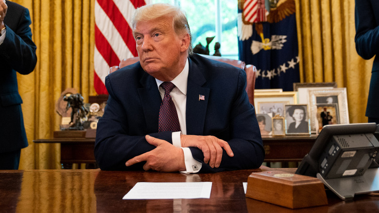 Donald Trump intently listening to someone speak from behind the Resolute desk