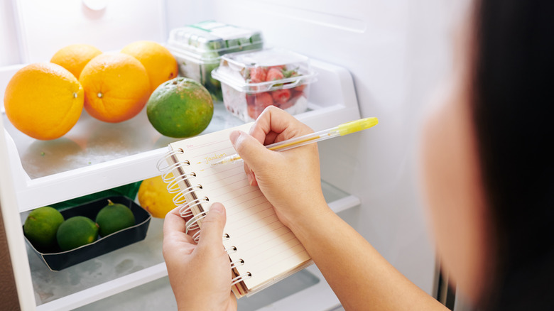 Woman checking her fridge and making a grocery list