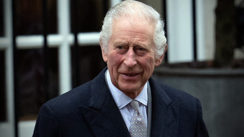 King Charles III smiling at the camera in a black suit