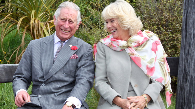 King Charles III and Queen Camilla laughing together while sitting on a bench