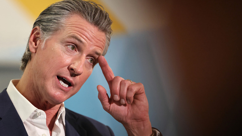 Gavin Newsom delivering a speech while touching his index finger to his head