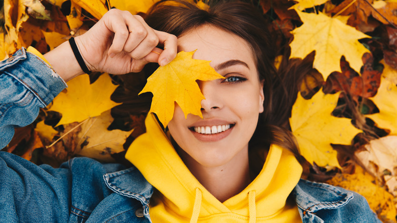 Woman lying in autumn leaves holds one over eye