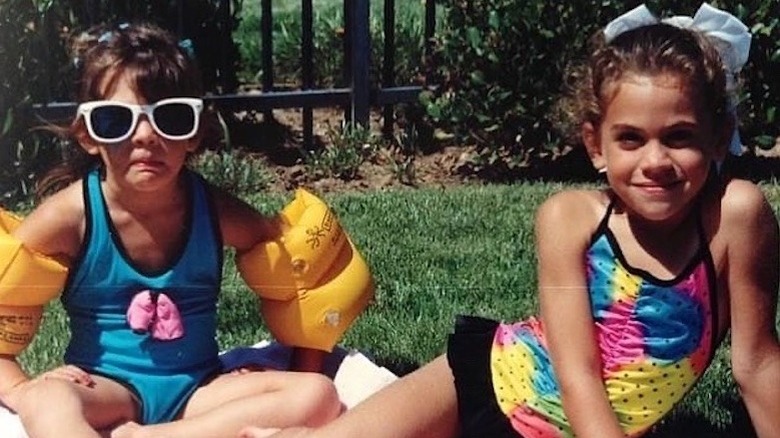 A young Kate Mansi wearing sunglasses next to her sister