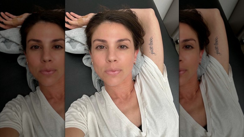 Kate Mansi lays with her arm above her showing off her sentimental tattoo with a contemplative look on her face wearing a tshirt