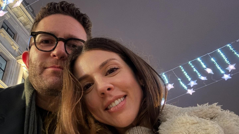 Kate Mansi smiles in in a selfie outside next to her husband with star lights in background