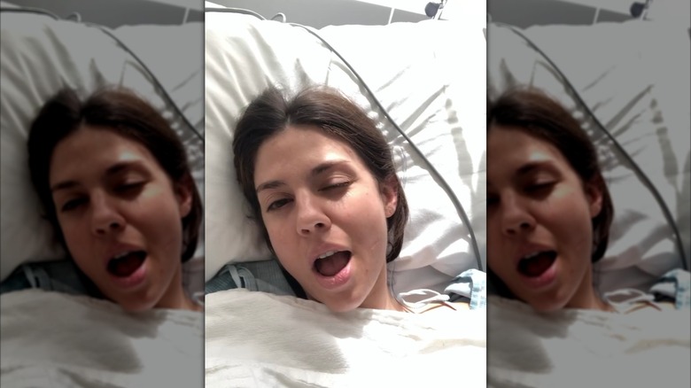 Kate Mansi winks as she lays in a hospital bed with a wire above her