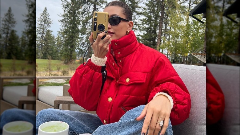 Hailey Bieber in red puffer jacket and sunglasses holding a film camera