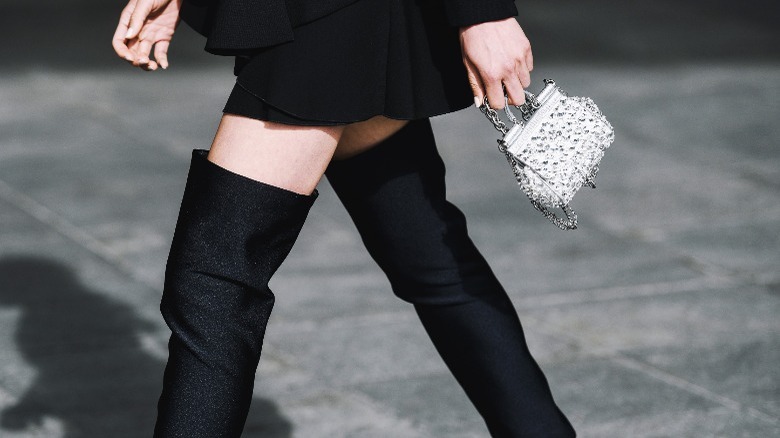 Woman wears black over-the-knee boots with white purse