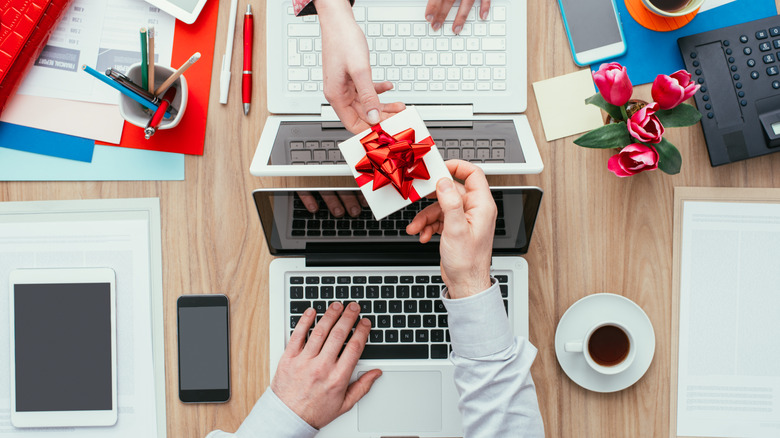 hands exchanging gift over laptops