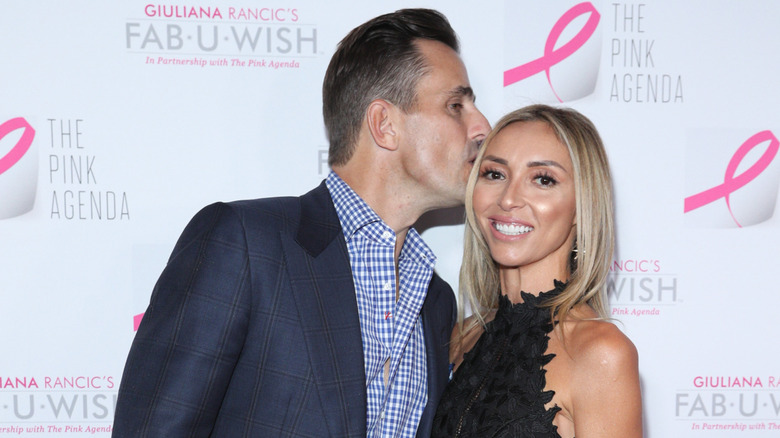 Bill Rancic kissing a smiling Giuliana Rancic on the head while they pose together on the red carpet