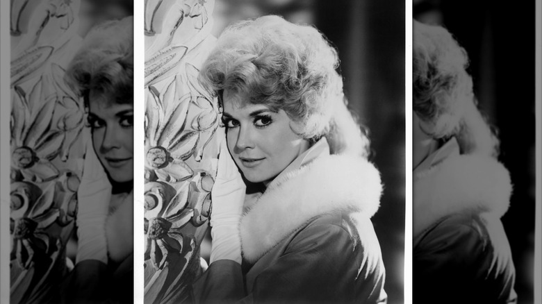 Donna Douglas posing near a carved pillar with a white fur collar on