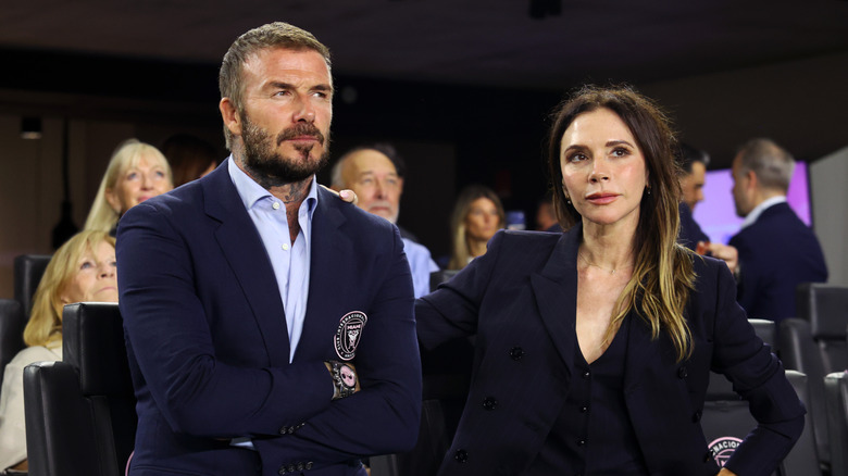 David Beckham in a blue suit and Victoria Beckham in a black suit posing side by side