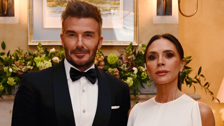 David Beckham wearing a tuxedo and Victoria Beckham wearing a white dress posing side by side