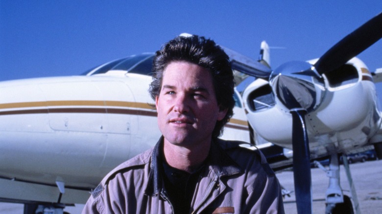 Kurt Russell posing in front of an airplane