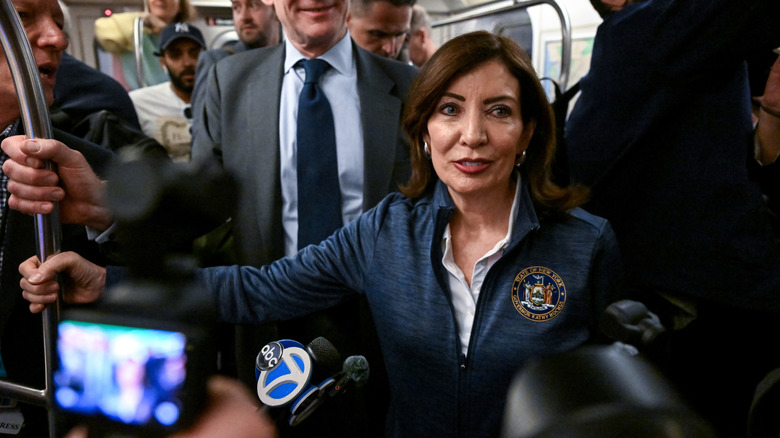 Kathy Hochul in a crowded train car, surrounded by microphones.