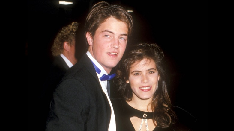 Matthew Perry wearing a blue bowtie and looking to the side while Tricia Leigh Fisher smiles beside him.