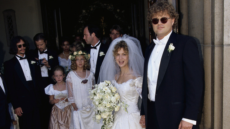 Tracey Gold and Roby Marshall in their wedding attire with guests behind them.