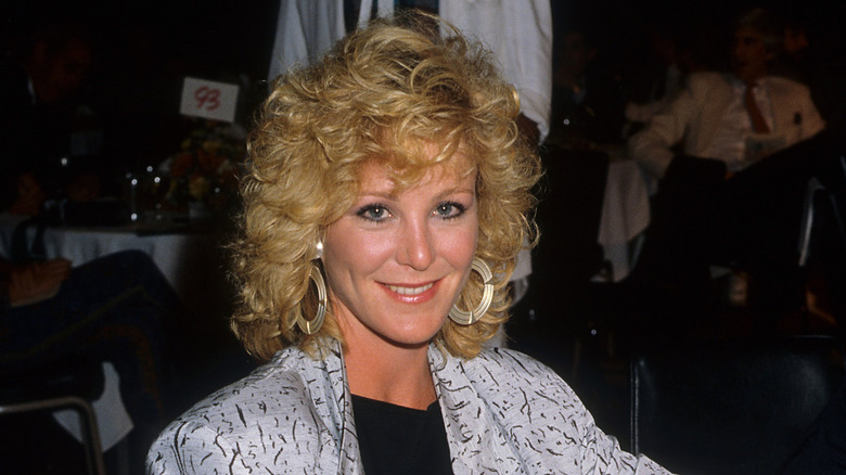 Joanna Kerns smiles in a whiite and black patterned blazer and big hoop earrings