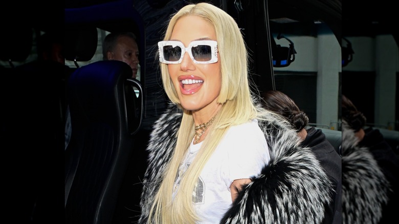 Gwen Stefani in white tee shirt and fur coat with white sunglasses and jellyfish haircut smiling