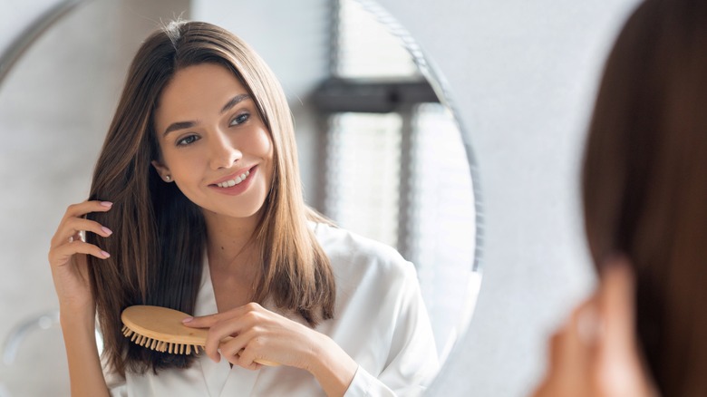 Woman staring at herself in a mirror while brushing her hair