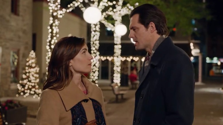 Carly Pope and Kristoffer Polaha talking to each other with Christmas lights in the background