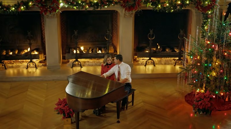 Bethany Joy Lenz and Kristoffer Polaha sitting at a piano in a room decorated for Christmas