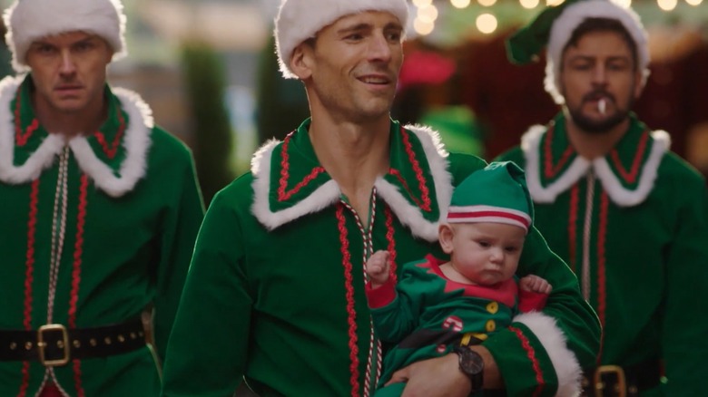 Andrew Walker holding a baby while Paul Campbell and Tyler Hynes walk behind them, all in elf costumes