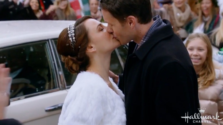 Princess in white fur shrug and tiara kissing man outdoors
