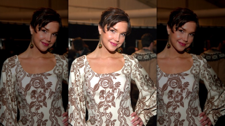 Arielle Kebbel poses in a romantic ivory and cream floral dress with her brown pixie cut laying smooth with a thin headband