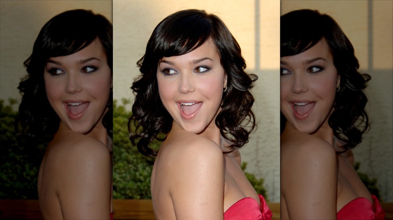 Arielle Kebbel looks over her shoulder with a playful smile with curled, shoulder length brown hair and micro bangs
