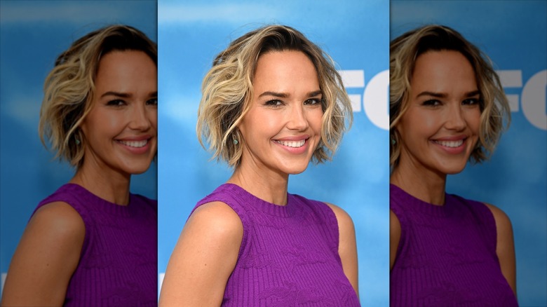 Arielle Kebbel smiling at the camera on a FOX red carpet in a wavy, bleached blond bob