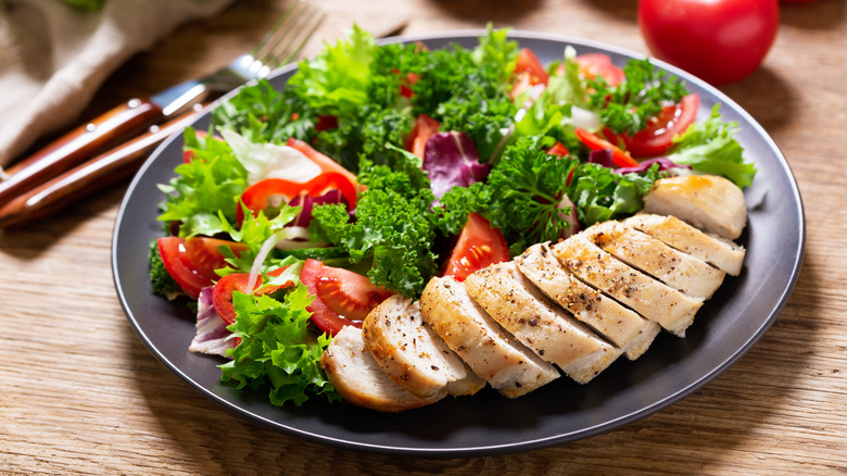 A green salad with tomatoes with a side of chicken