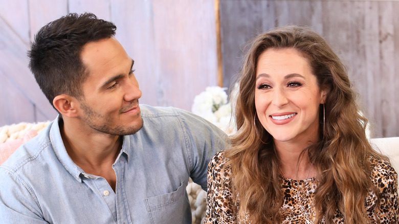 Carlos and Alexa PenaVega sitting on a couch in front of a wood-paneled background