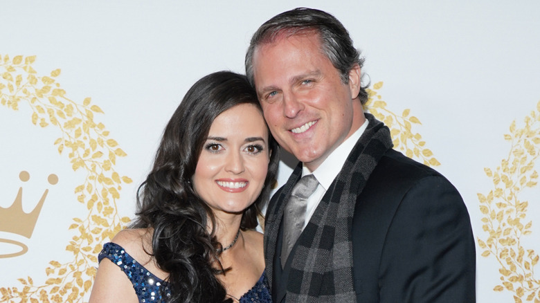"Perfect Match" actor Danica McKellar smiles at a Hallmark event wearing a blue sparkling dress with Scott Sveslosky who smiles wearing a suit and scarf