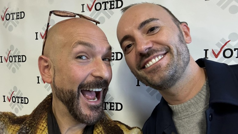 Actor Marco Soriano smiling in a selfie with husband Michal Le Fou in front of an "I Voted" banner