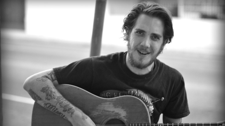 Black and white photo of Malcolm Ford posing with a guitar in 2013