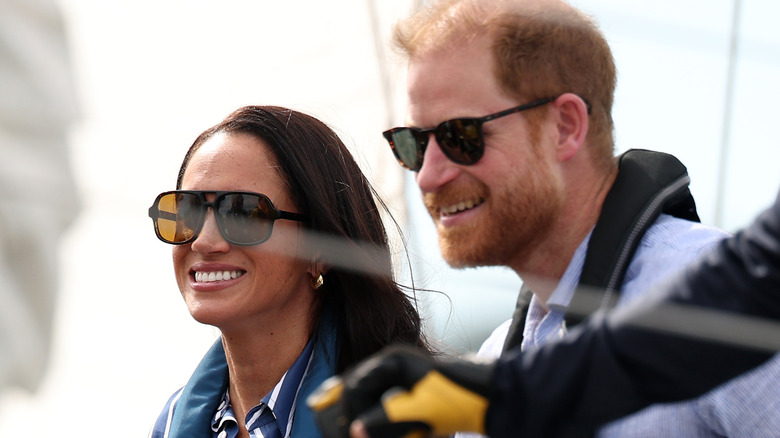 A smiling Meghan Markle and Prince Harry smiling while wearing sunglasses