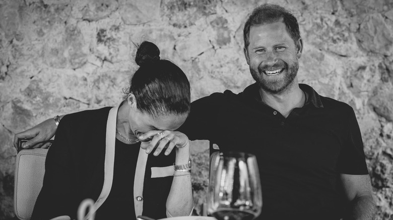 b/w photo of Meghan Markle laughing next to Prince Harry at dinner table