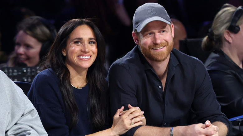 Meghan holding Harry's arm while sitting in stands