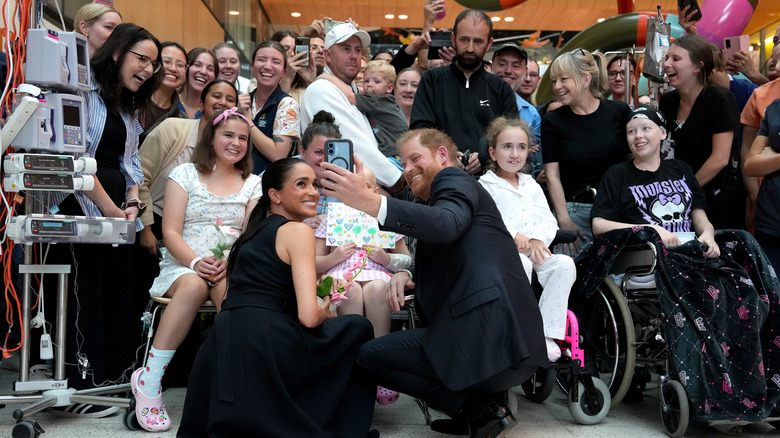 Meghan Markle and Prince Harry take pictures with patients in a children's hospital.