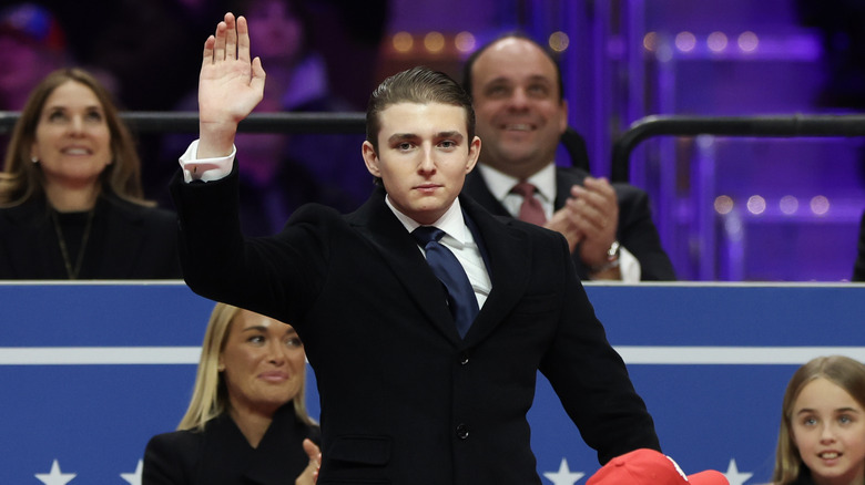 Barron Trump waving in a black suit with a navy tie