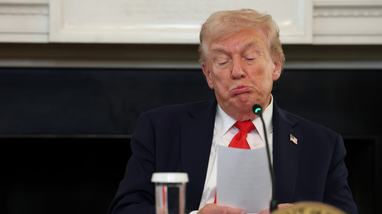 Donald Trump frowning while looking down at a piece of paper.