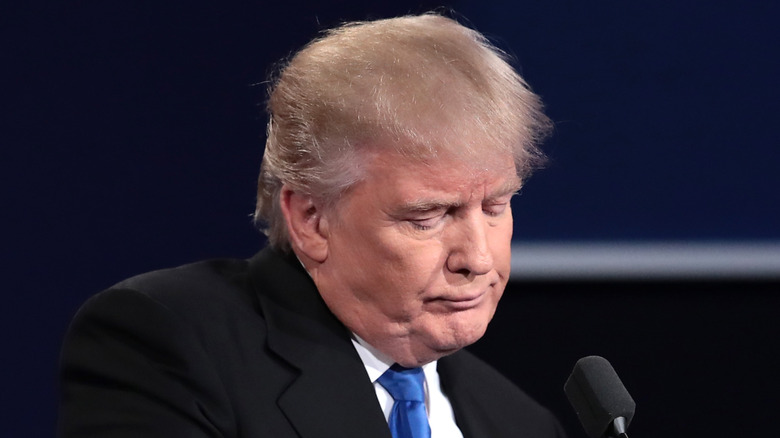 Donald Trump looking sad behind a podium in a suit