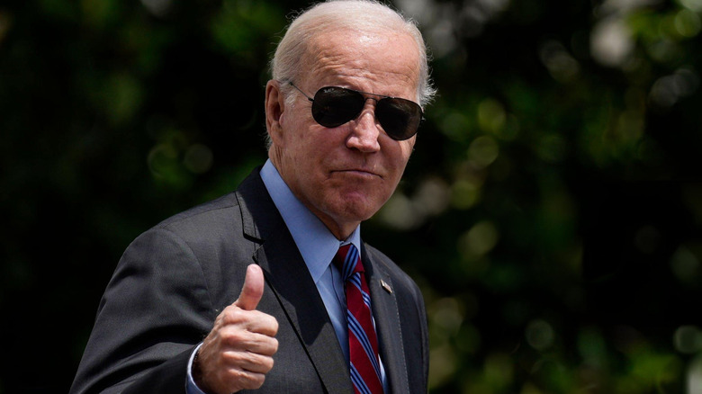 Joe Biden wearing sunglasses and a suit while giving photographers a thumbs-up